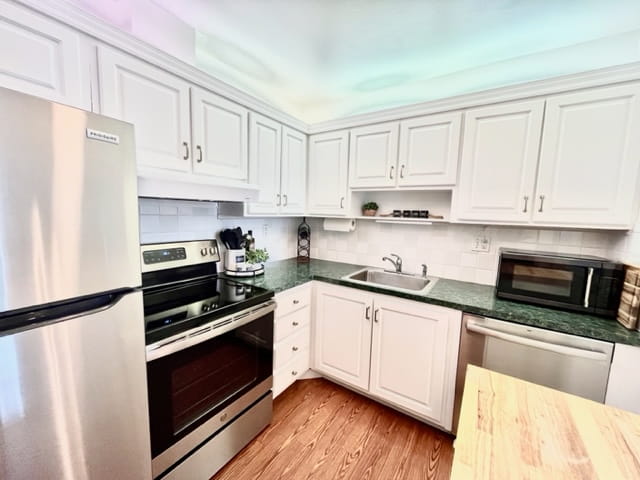 Image de la cuisine du condo situé à margate.  Les armoires sont blance et il u y un petit comptoir lunc dans le coin droit et on voit bien les électroménager dans la cuisine. Ils sont en stainless.